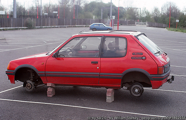 A red compact car with no tires or wheels propped up on bricks.